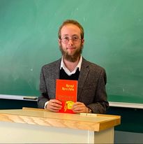 Image of a bearded man in glasses holding a copy of the book Quicksand/Stargazing