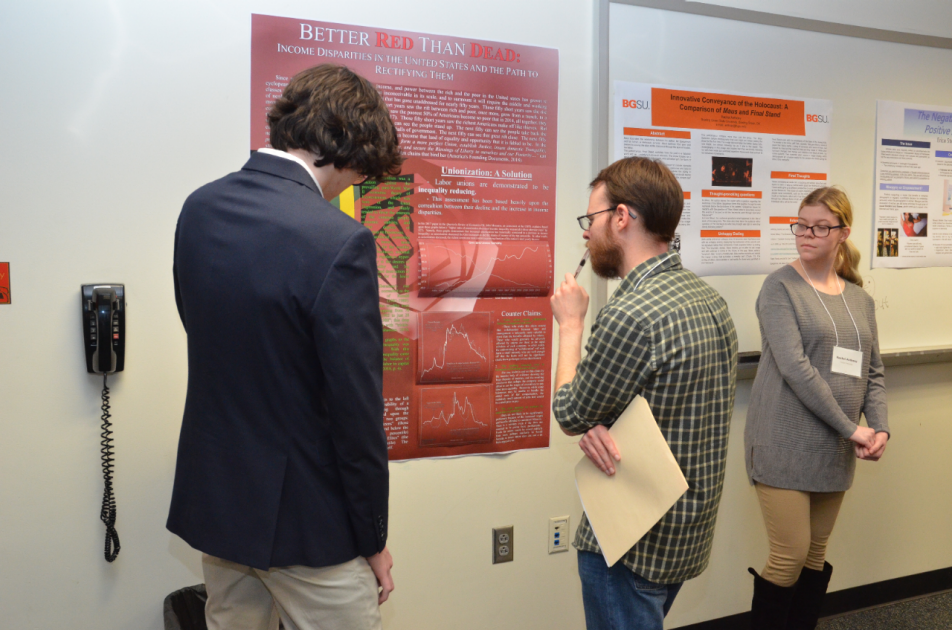 Presenters and attendees from a previous Writing Showcase discuss a poster presentation